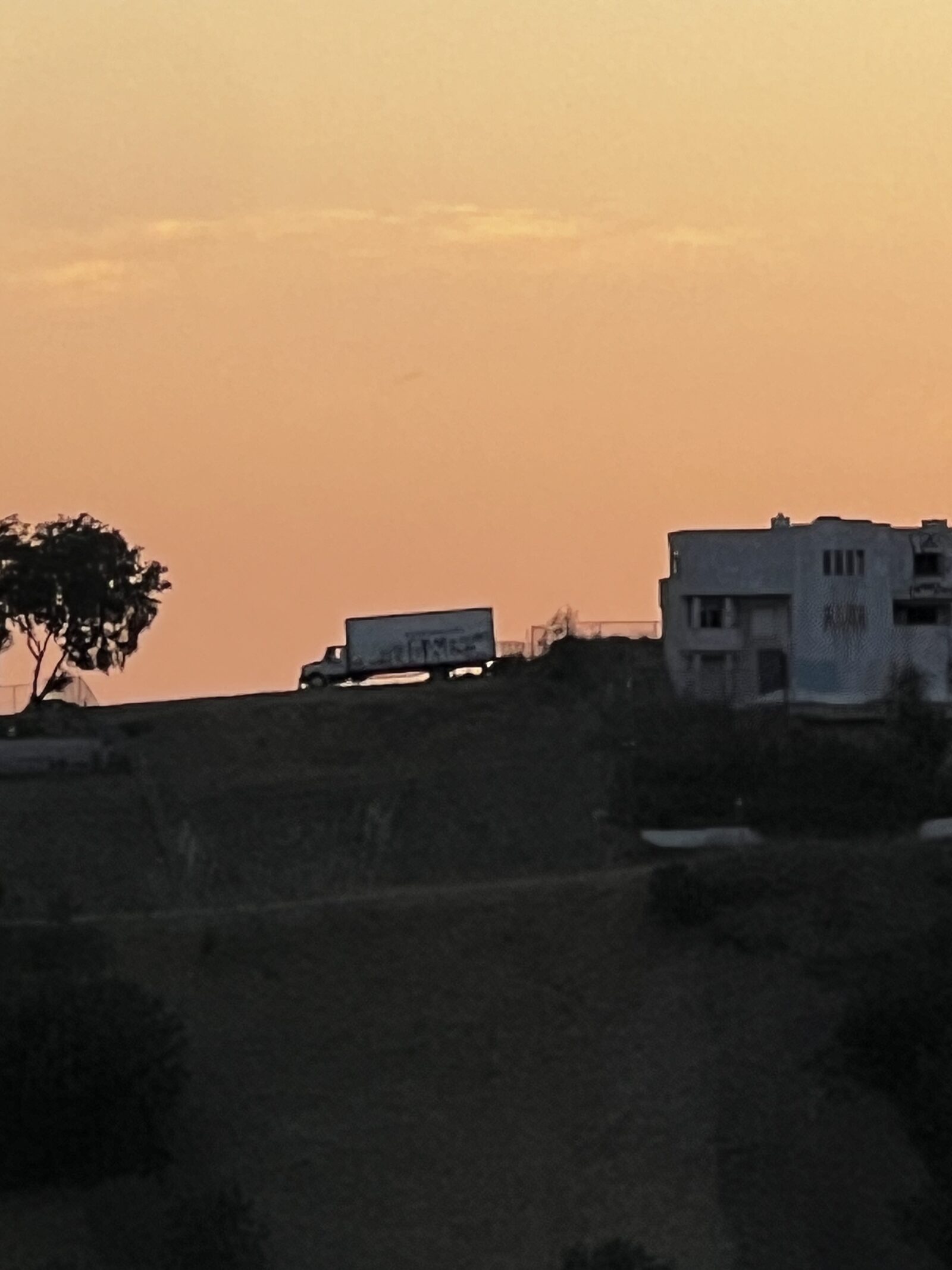 Silhouette of a trailer and a building on the opposite ridge, backlit by an orange sunset.